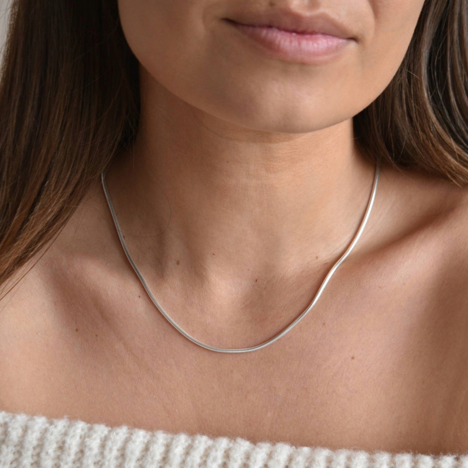 Angled close-up of a sterling silver snake chain necklace, showing its slim, polished profile against the skin.
