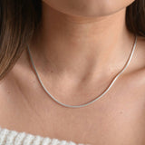 Sterling silver snake chain necklace worn below the collarbone, showing its smooth curve across the neckline.